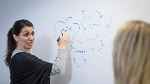 En kvinna skriver på en whiteboard med en tuschpenna.