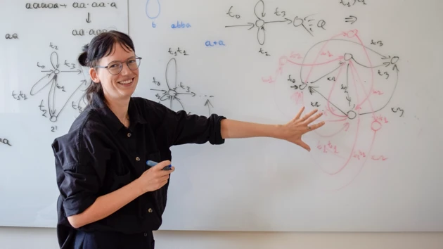 Bild på Willeke Martens stående vid whiteboardtavla med formler och figurer