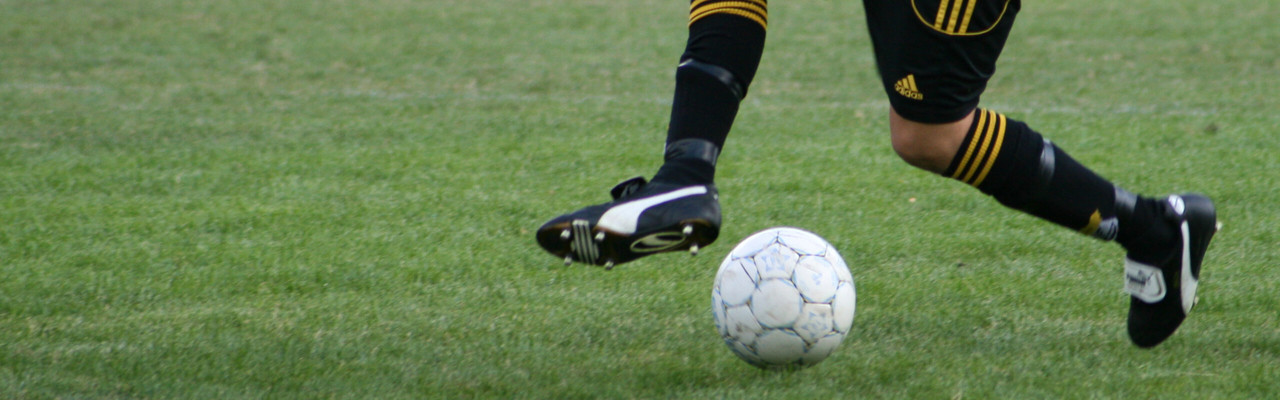 Detaljbild på person som dribblar med en fotboll på en gräsplan.