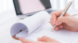 Hand med penna som ska kryssa i svar i en enkät. Bilden ska illustrera enkäter, mätningar, utvärdering.