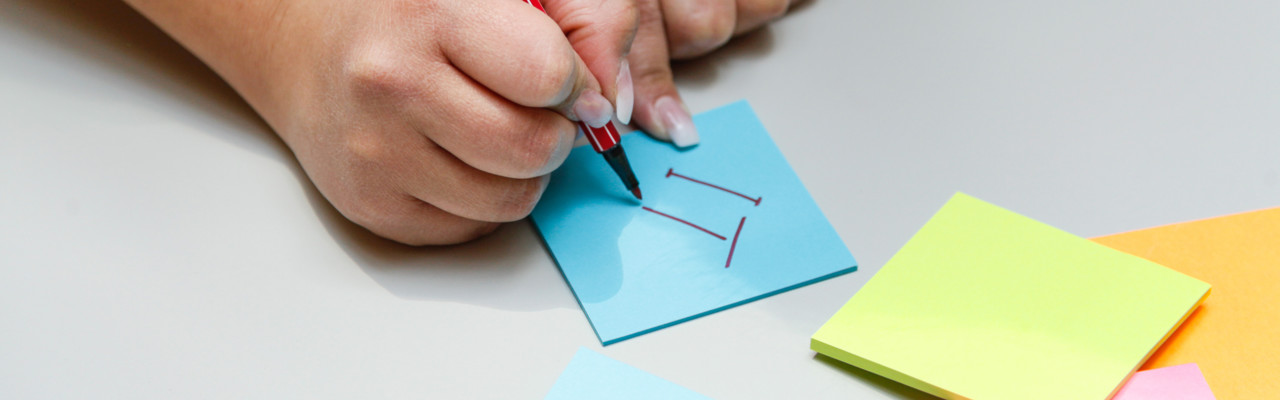 Hand som skriver IT på en post-it-lapp.
