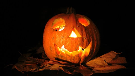 Halloweenpumpa med utskurna ögon och mun med ljus inuti på kvällen/natten.