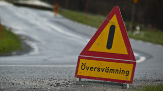 Bild på varningsskylt med texten Översvämning som står på en väg.