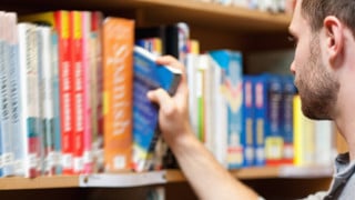 Yngre man väljer ut en bok ur bokhyllan på ett bibliotek.