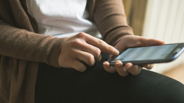 Detalj på person vars händer håller i en mobiltelefon som hen surfar på.