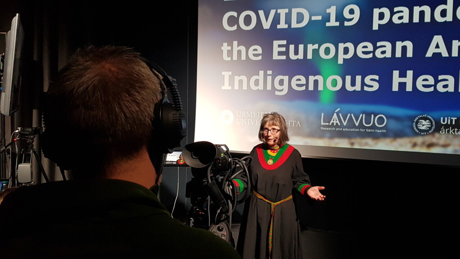 Woman in traditional Sámi garb stands in front of camera