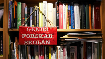 Broderad skylt där det står "Genusforskarskolan" hänger på en bokhylla
