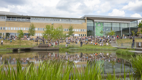 Vy över dammen mot folksamling utanför Lindellhallen, Umeå universitet.