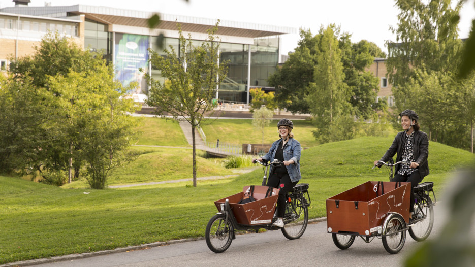 Två personer med eldriva lådcyklar som hyrs ut av Umeå kommun på campus.