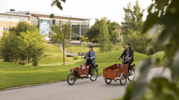 Två personer med eldriva lådcyklar som hyrs ut av Umeå kommun på campus.