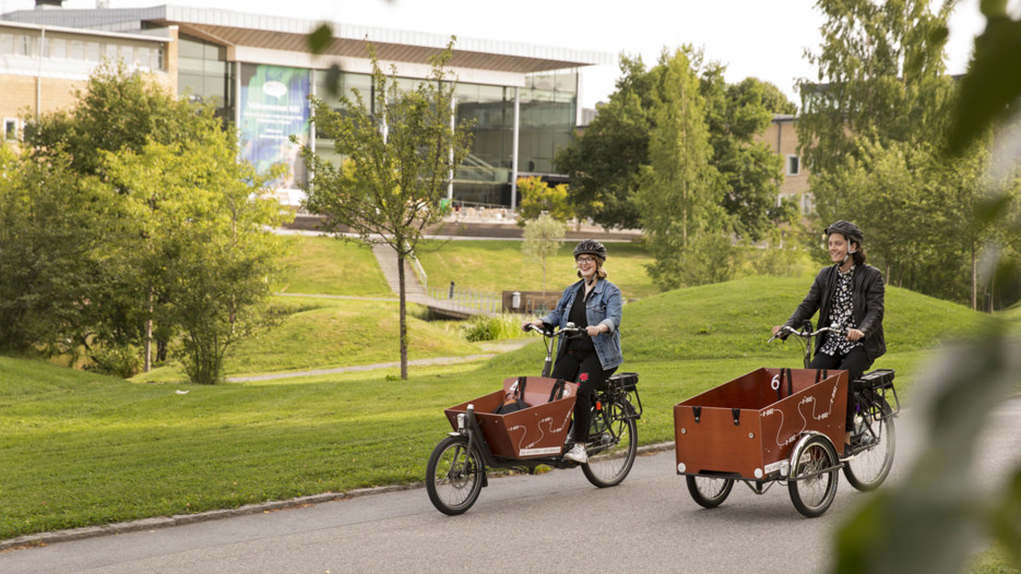 Två personer med eldriva lådcyklar som hyrs ut av Umeå kommun på campus.