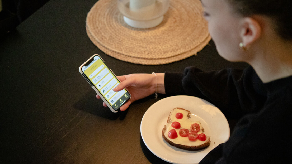Kvinna sitter vid ett bord med en mobiltelefon i handen och planerar sin träning