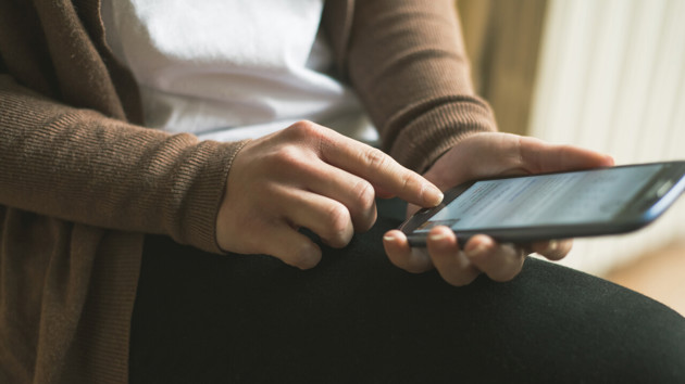 Detalj på person vars händer håller i en mobiltelefon som hen surfar på.