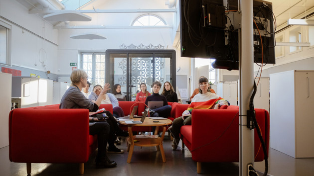 Tio personer sitter samlade runt ett bord. En talar och gestikulerar medan de andra lyssnar koncentrerat. I högra kanten syns baksidan av en monitor.